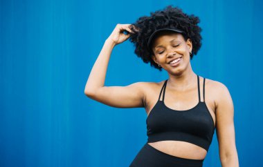 Mavi arka planda duran neşeli genç bir kadının portresi, antrenman sırasında mola veriyor..