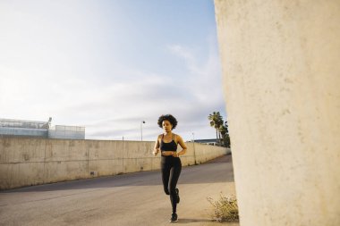 Sabahın erken saatlerinde şehir ortamında koşan genç bir kadın spor kıyafetleri giyiyor..