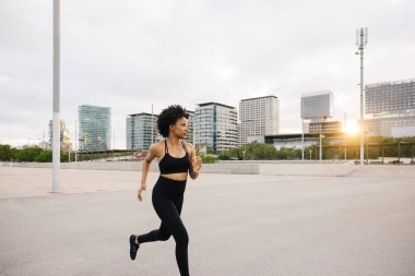 Bulutlu bir günde gün batımında şehir ortamında koşan kararlı genç bir kadın..