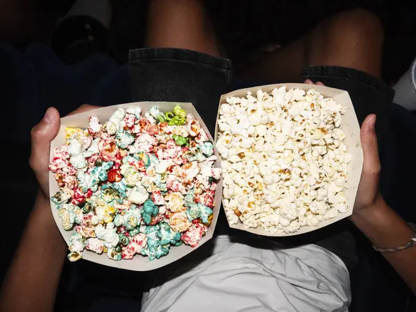 stock image Boy holding two containers of popcorn, one filled with sweet and colorful popcorn and the other with plain, classic popcorn, while waiting in the cinema.