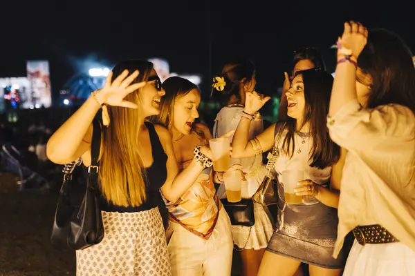 stock image Group of young women dancing and enjoying their drinks at an outdoor music festival at night.