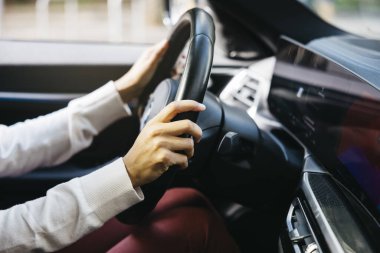 Bir insanın elleri elektrikli bir arabanın direksiyonunu sıkıca tutarken modern teknolojiyi ve çevre dostu otomotiv tasarımını sergiliyor..