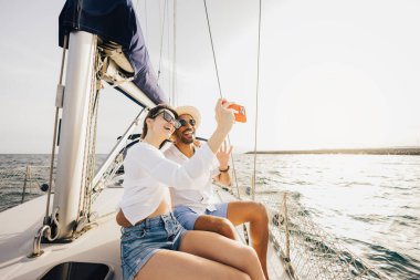 Mutlu çift, bir yelkenlide rahatlatıcı bir günün tadını çıkarıyor. Selfie ile anılarını yakalıyorlar. Güneş sakin denizin üzerinde ışıldıyor, neşeli ve huzurlu bir atmosfer yaratıyor..