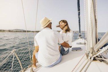 Neşeli bir çift, sakin okyanus manzarasıyla çevrili bir yelkenlide güneşli bir günün tadını çıkarıyor. Sahne romantizmi, rahatlığı ve macerayı yakalar..