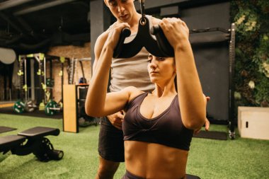 Kararlı bir kadın modern bir spor salonunda kişisel antrenörünün rehberliğinde egzersiz yapıyor. Güç eğitimi ve takım çalışması odak ve zindelik atmosferini vurgular.