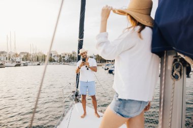 Neşeli bir çift yelkenlide dinleniyor, marinada güneşli bir günün tadını çıkarırken akıllı bir telefonla anılarını yakalıyor. Boş zaman, seyahat ve romantizm kavramları için mükemmel..