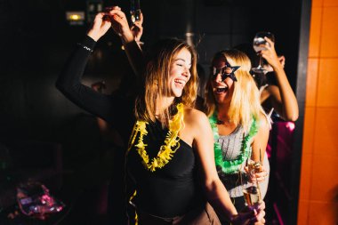 İki neşeli arkadaş renkli aksesuarlar giyerek şenlikli bir partinin tadını çıkarıyor. Kadehleri kaldırır, güler ve neşeli atmosferi kucaklarlar..