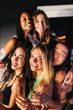Neşeli bir grup genç kadının portresi, duruma uygun giyinmiş, neşeli bir partide şampanyayla mutlu bir şekilde kutlanıyor..