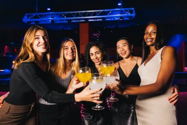 Group picture of joyful friends enjoying cocktails and smiling brightly at a lively nightclub. They are laughing and toasting with colorful cocktails, capturing a moment of celebration. clipart