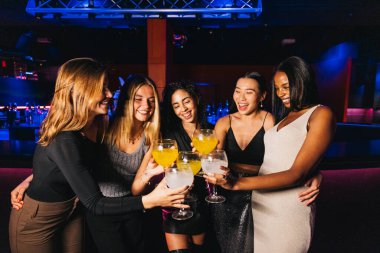 Canlı bir gece kulübünde eğlenen neşeli bir grup genç arkadaş. Renkli kokteyllerle gülüyor ve kadeh kaldırıyorlar. Bir kutlama anı yakalıyorlar..