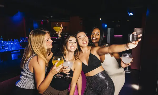 Dört genç bayandan oluşan bir grup canlı bir partide içki içerken mutlu bir şekilde selfie çekiyorlar..