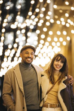 Neşeli bir çift, bayram ruhunu kucaklayarak bayram ışıklarının gölgesinde Noel alışverişinin tadını çıkarıyor..