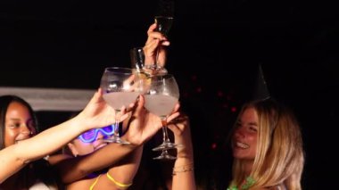 Canlı bir gece kulübünde eğlenen neşeli bir grup genç arkadaş. Renkli kokteyllerle gülüyor ve kadeh kaldırıyorlar. Bir kutlama anı yakalıyorlar..