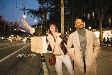 Neşeli bir çift alışveriş yaptıktan sonra bir şehir caddesinde duruyor, bir taksi çağırmaya çalışıyorlar, hayat dolu bir şehir akşamının tadını çıkarıyorlar, sokak lambaları manzarayı aydınlatıyor..