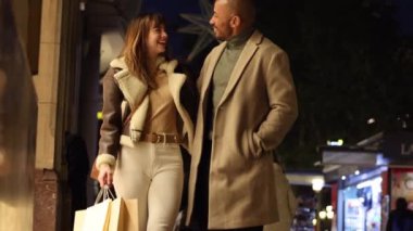 Neşeli çift şehir sokaklarında gezer, alışveriş yapar ve dışarıda romantik bir akşam geçirir. Gülümsüyorlar, alışveriş torbalarını tutarken sevgi gösteriyorlar..