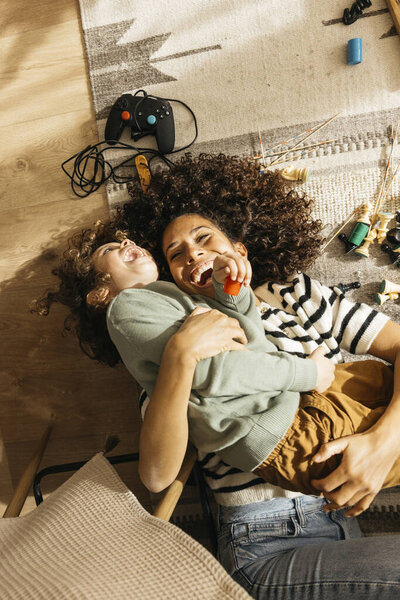 A cheerful mother and her young son share joyful moments playing on the living room floor, surrounded by toys showcasing family bonding and happiness.
