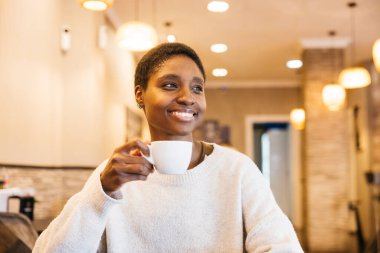 Sıcak, davetkar bir kafede bir fincan kahveyle rahatlayan bir kadın.