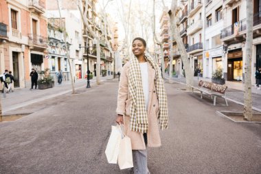Elinde alışveriş torbalarıyla yaya caddesinde yürüyen mutlu bir müşteri.