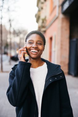 Neşeli genç bir kadın sokakta yürürken hoş bir telefon konuşması yapıyor.