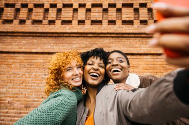 Üç neşeli bayan turist, duvarın önünde akıllı telefonlarıyla selfie çekiyorlar. Seyahat maceralarının tadını çıkarıyorlar.