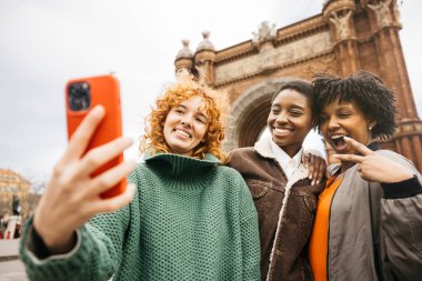 Barcelona, İspanya 'da Arc de Triomf' un önünde akıllı telefonla selfie çeken üç mutlu bayan turist.