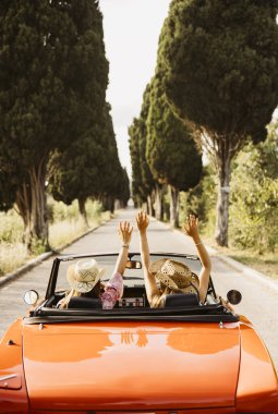 İki turist yaz yolculuğunun tadını çıkarıyor, kolları havada, üstü açık klasik bir araba kullanıyorlar.