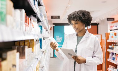 Eczacı ilaç kutusu tutuyor ve eczanede dijital tablet kullanıyor.