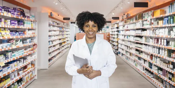 Kendine güvenen eczacı gülümsüyor, elinde dijital tablet tutuyor ve modern bir eczanede envanter yönetiyor.