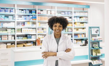 Bir eczanede kollarını kavuşturarak poz veren gülümseyen eczacının portresi, sağlık hizmetlerinde güven ve profesyonellik gösteriyor.