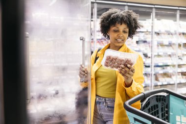 Kadın süpermarketteki buzdolabında kıyma paketi seçiyor.
