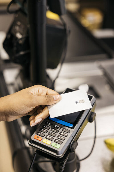 Customer using contactless payment with credit card at POS terminal in supermarket checkout
