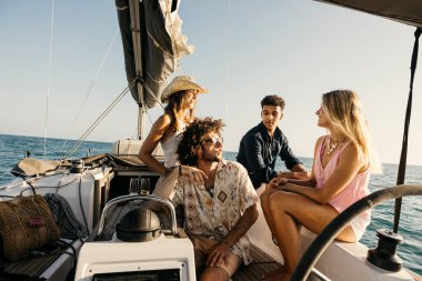 Bir grup arkadaş güneşli bir günde okyanusta yelkenliyle gezmenin keyfini çıkarıyorlar.
