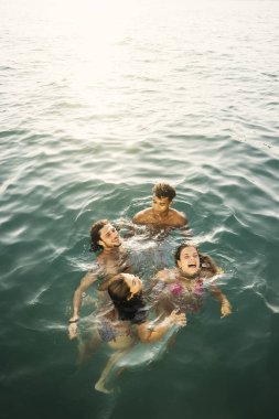 Bir grup neşeli genç arkadaş yaz tatili boyunca denizde birlikte banyo yapıyorlar.