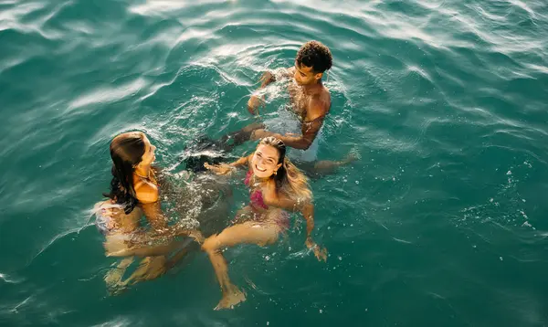 Bir grup arkadaş yaz tatilinde berrak turkuaz okyanus suyunda birlikte yüzüyorlar.