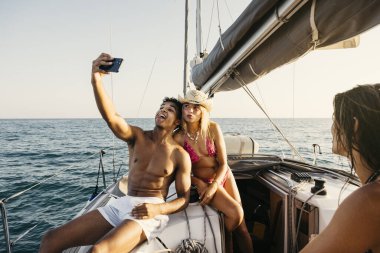 Yaz tatilinde yelkenliyle selfie çeken turistler, denizde arkadaşlığın ve maceranın tadını çıkarıyorlar.