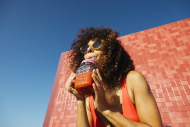 Neşeli genç bir kadın sahilde bir yaz günü taze meyve suyu içiyor.