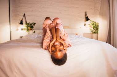 Genç bir kadın yatakta baş aşağı yatıyor, gülümsüyor ve odasında mutlu hissediyor.