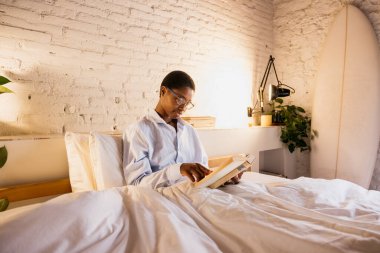 Evde yatakta rahat bir şekilde uzanmış kitap okuyan bir kadın, boş vakitlerin tadını çıkarıyor.