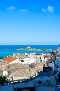 Vieste, İtalya. Via Cesare Battisti 'den kasaba manzarası. Uzakta Vieste 'nin deniz feneri. Dikey görüntü. 5 Eylül 2022.