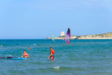 Vieste, İtalya. Scialmarino sahilinin yakınında rüzgar sörfçüsü ve banyo yapıyor. Arka planda Tufara Körfezi ve Porticello Kulesi 'nin trabucco' su var. Vieste sahilinde bir yaz günü. 7 Eylül 2022