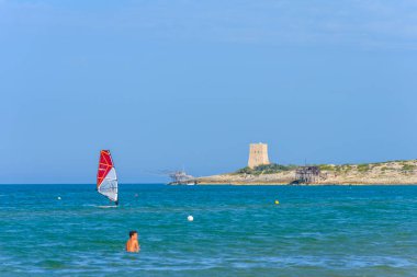 Vieste, İtalya. Scialmarino plajı yakınlarında rüzgar sörfçüsü. Arka planda Tufara Körfezi ve Porticello Kulesi 'nin trabucco' su var. Vieste sahilinde bir yaz günü. 7 Eylül 2022