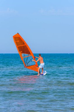 Vieste, İtalya. Scialmarino sahilinin yakınındaki Vieste denizinde genç bir adam kırmızı bir rüzgar sörfü ile rüzgar sörfü yapıyor. Dikey görüntü. 7 Eylül 2022