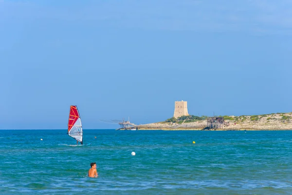 Vieste, İtalya. Scialmarino plajı yakınlarında rüzgar sörfçüsü. Arka planda Tufara Körfezi ve Porticello Kulesi 'nin trabucco' su var. Vieste sahilinde bir yaz günü. 7 Eylül 2022