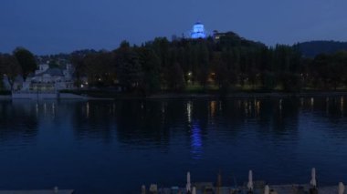 Torino, İtalya. Santa Maria al Monte dei Cappuccini Kilisesi 'nin mavi ışıkla aydınlatıldığı gece manzarası. Ön plandaki Po Nehri. Gerçek zamanlı video. 29 Ekim 2022.