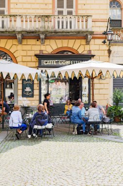Torino, İtalya. Piazza della Consolata 'da, büyük şemsiyelerin altında, kafeteryanın açık masalarında bazı insanlar oturuyor. Dikey görüntü. 2023-05-04.