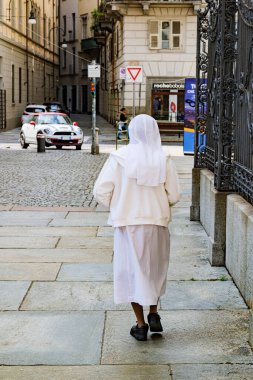Torino, İtalya. Beyaz elbiseli rahibe, tarihi merkezdeki Consolata Kilisesi 'nin yakınında yürürken arkadan görülüyor. 2023-05-04.