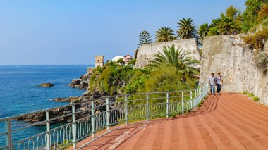 Ceneviz, İtalya. Cenova yakınlarındaki Nervi kıyısında, iki insan, baba ve oğul, güneşli bir günde, denize bakan kırmızı tuğla Anita Garibaldi gezinti güvertesi boyunca yürüyorlar. 2023-10-06.