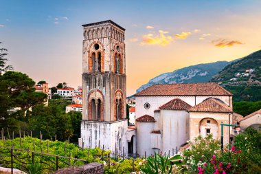 Ravello, İtalya. Santa Maria Assunta Katedrali 'nin üzerinde nefes kesici bir gün batımı ve çiçeklerle renkli zakkum çiçekleri arasındaki çan kulesi. 2020-08-09.