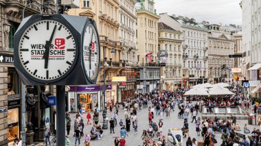 Viyana, Avusturya. Stock-im-Eisen-Platz Meydanı 'nın yukarısı insan ve turistlerle dolu. Şehir merkezindeki alışveriş alanında. Ön planda dört düğmeli bir sokak saati var. 2023-08-03.