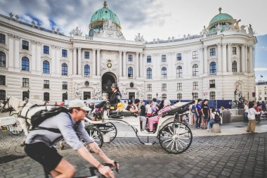 Viyana, Avusturya. Tarihi binası olan Michaelerplatz şimdi İspanyol Binicilik Okulu 'na ev sahipliği yapıyor. Önde bir turist arabası ve bisikletli bir bisikletçi var. 2023-08-02.